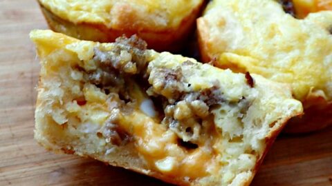Three easy muffin tin sausage quiche cups on a wooden cutting board with one cut in half down the middle