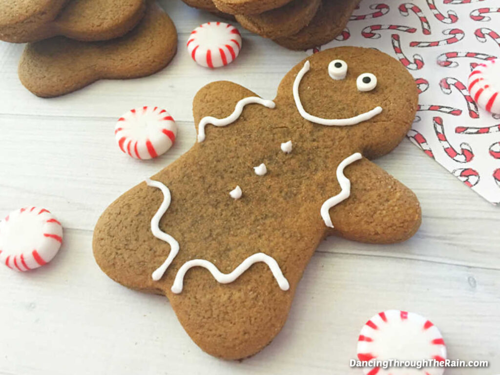 An Easy Gingerbread Man on a white table surrounded by peppermint candies next to a stack of more cookies