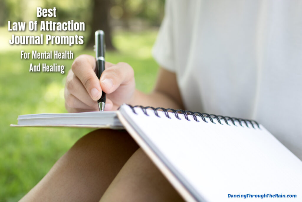 A white journal with someone writing in it with a pen while sitting on the lawn and wearing a white t-shirt with the words Best Law of Attraction Journal Prompts for Mental Health and Healing