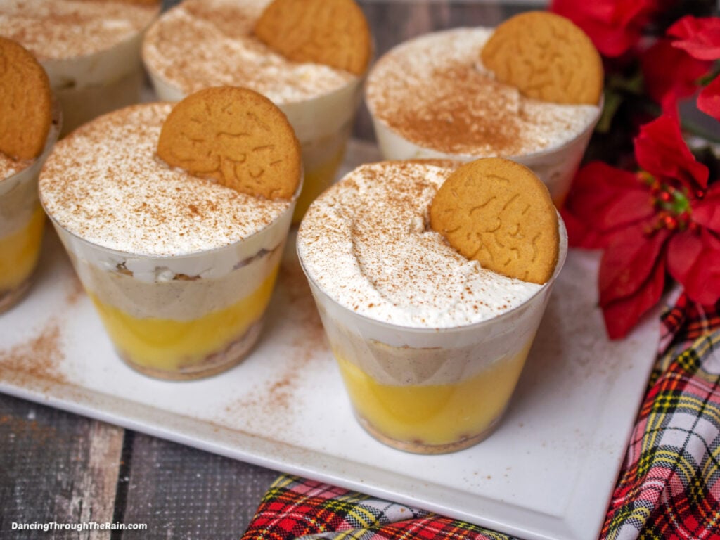 A white square platter full of No-Bake Gingersnap Cheesecake Cups next to red flowers on a gray wooden tabletop