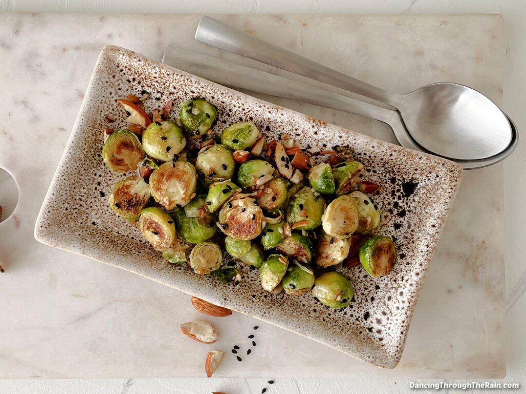 Pan Fried Almond Brussel Sprouts on a rectangular serving tray with a metal spoon