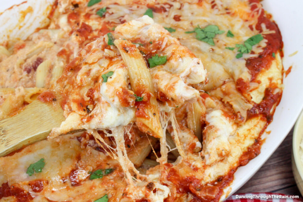 A closeup of Easy Cheesy Penne Pasta Bake with a wooden spoon lifting melted cheese and pasta out