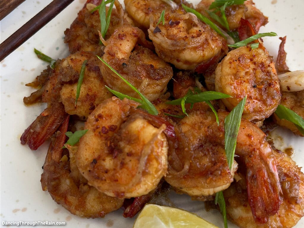A closeup of Hot Honey Shrimp on a white plate with a lemon wedge and wooden chopsticks