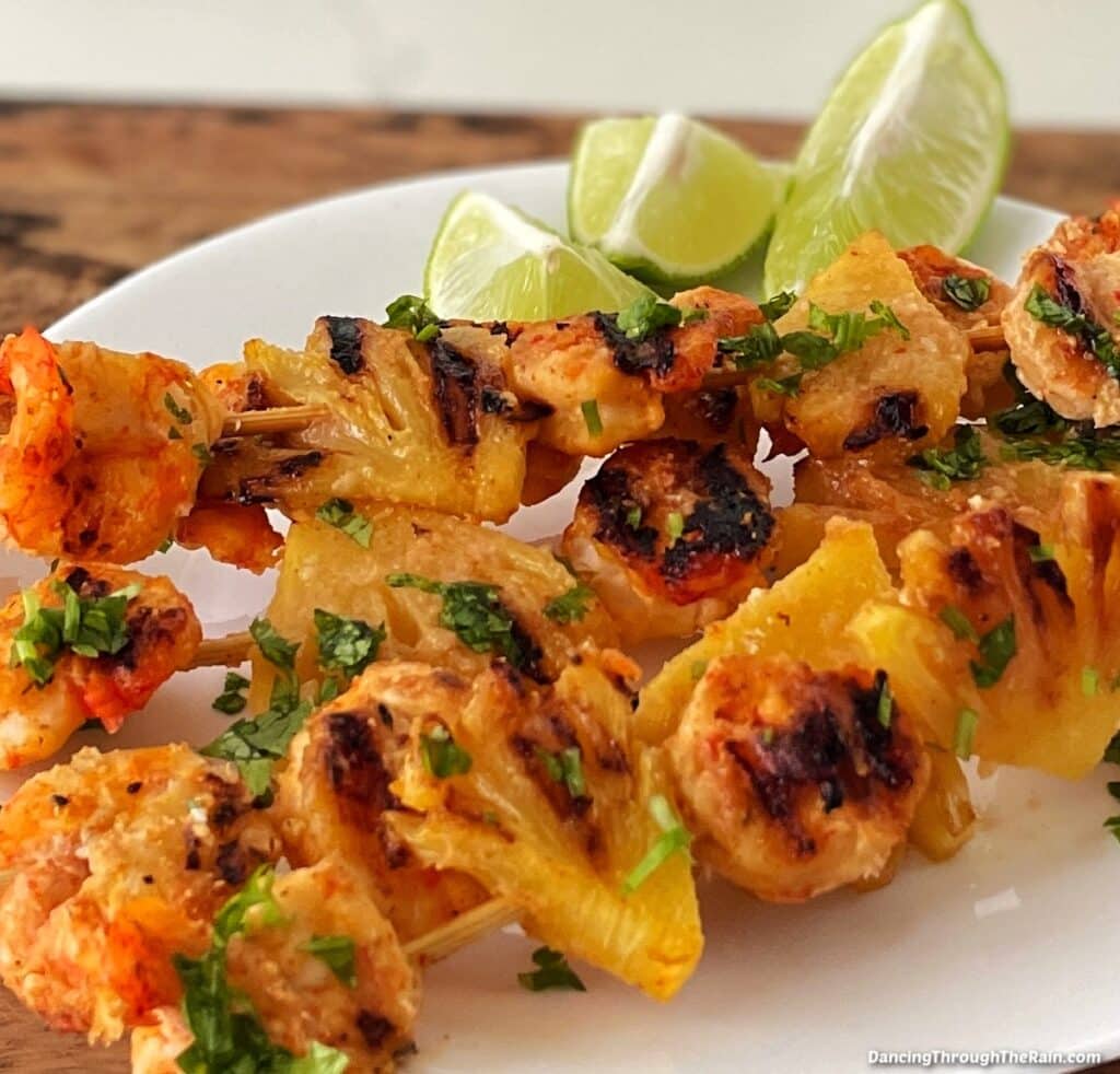 A closeup of Grilled Coconut Pineapple Skewers on a white plate with limes
